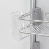 A close-up of a transparent plastic cup attached to a silver and clear plastic bathroom shelf unit, mounted on a light-colored wall. The shelf has a slatted design for drainage.
