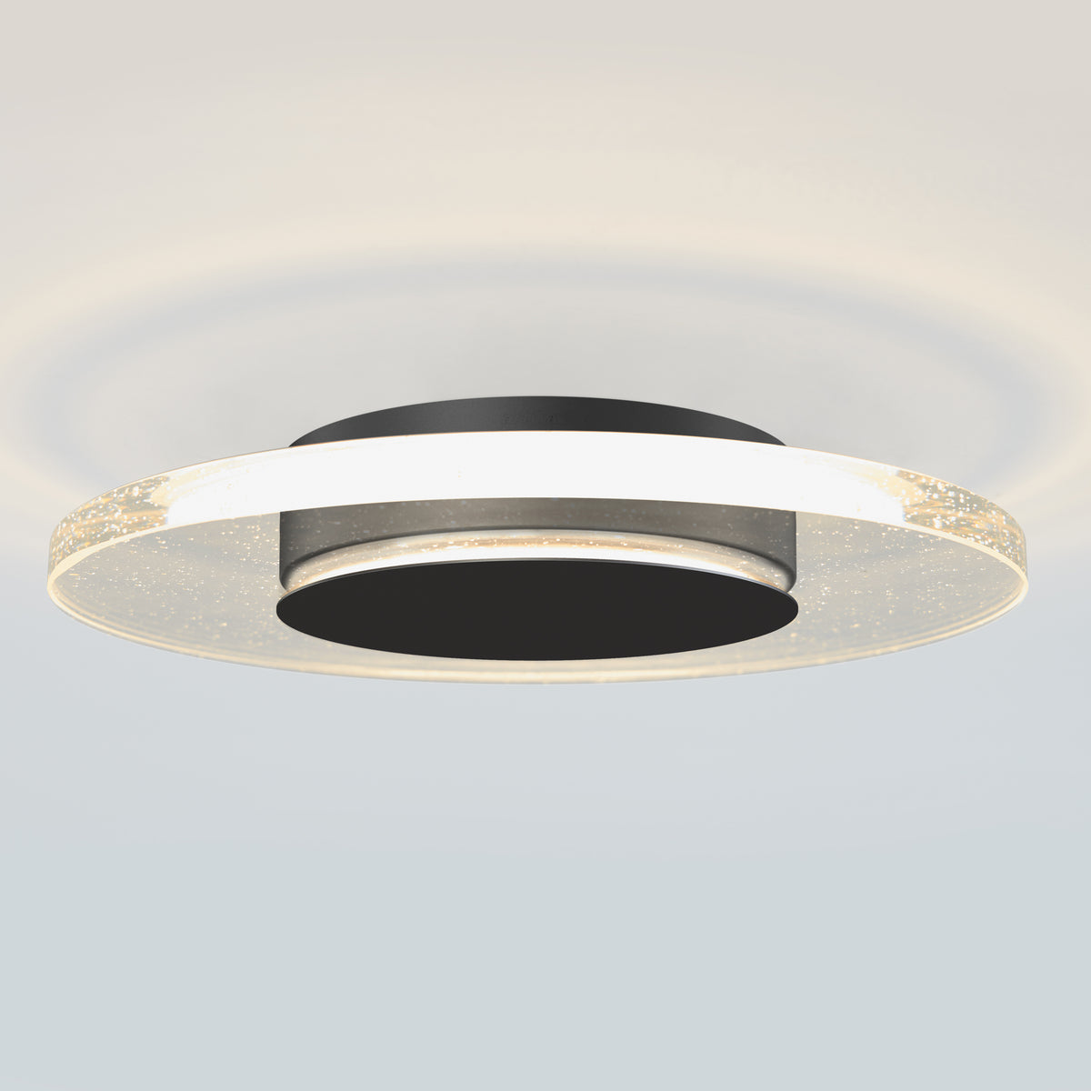 A modern, circular ceiling light fixture with a black center and a glowing, translucent outer ring featuring tiny embedded bubbles, casting soft illumination on the ceiling.