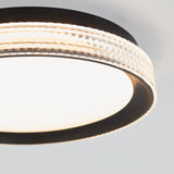 A modern circular ceiling light fixture with a frosted white center and a decorative, textured clear outer ring, emitting a soft, even glow. The fixture has black trim and is mounted on a white ceiling.