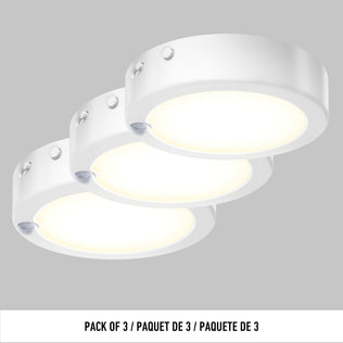 Three round, white Artika Accent under cabinet LED light 3CCT surface-mounted puck lights arranged in a row on a gray background. Text below reads: PACK OF 3 / PAQUET DE 3 / PAQUETE DE 3.