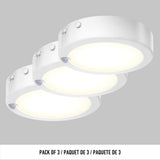Three round, white LED puck lights are shown illuminated, arranged in a staggered row against a grey background. Text below reads: Pack of 3 / Paquet de 3 / Paquete de 3.