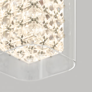A close-up of the Artika Crystal Cube 1-light LED pendant light, featuring geometric crystal patterns glowing warmly and partially encased in a clear curved glass panel, set against a light gray background.