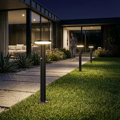 Artika’s Urbia Solar LED Bollard with Motion Sensor lights a dusk walkway as someone stands near the home’s entrance.