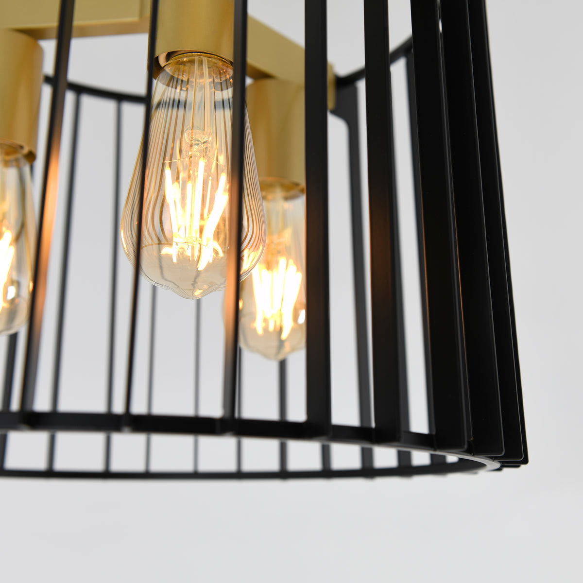 Close-up of exposed vintage-style light bulbs glowing inside a modern black metal and gold cage pendant light fixture against a plain white background.