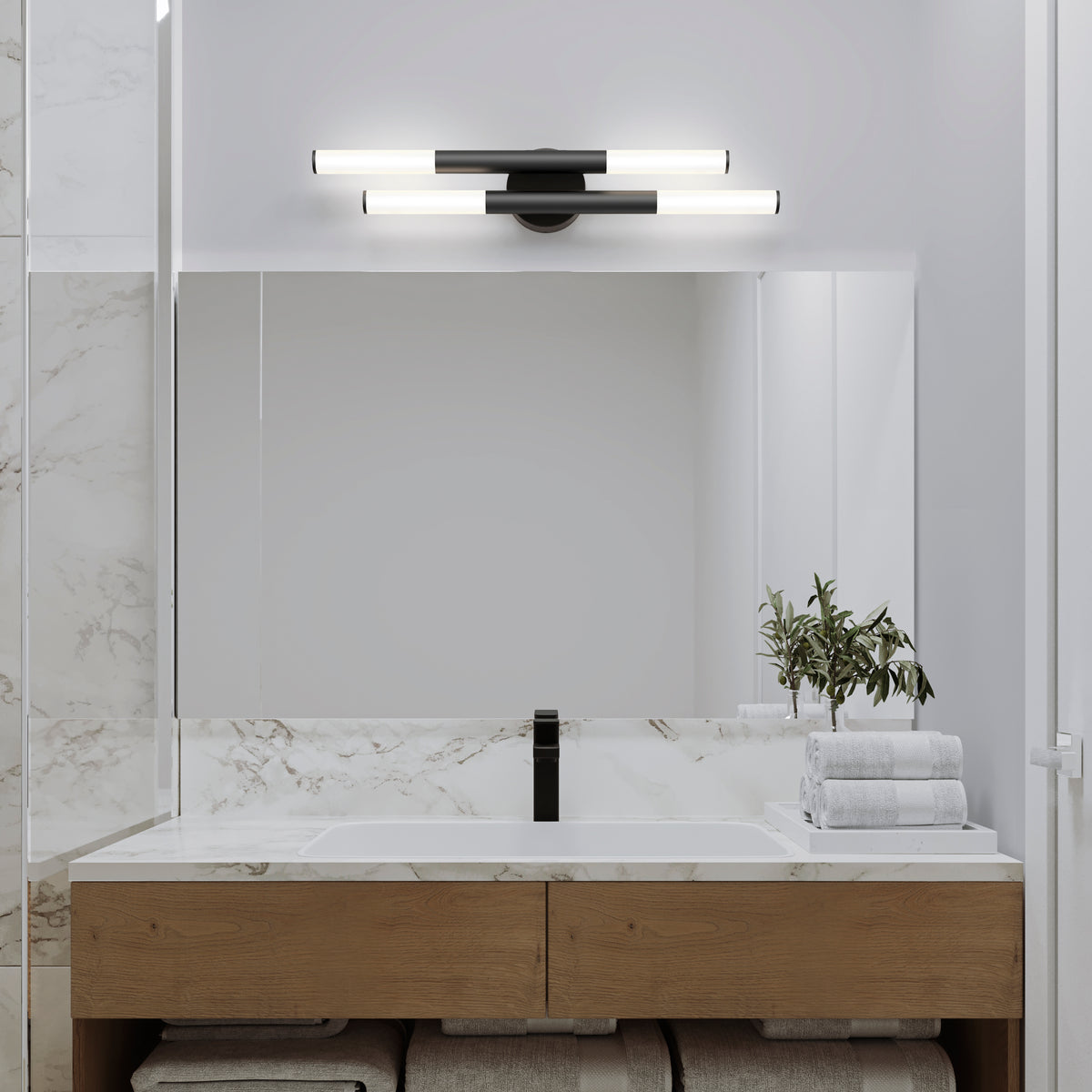 A modern bathroom with a large mirror, marble backsplash, wooden vanity, stacked white towels, a small plant in a glass vase, and two horizontal light fixtures above the mirror.