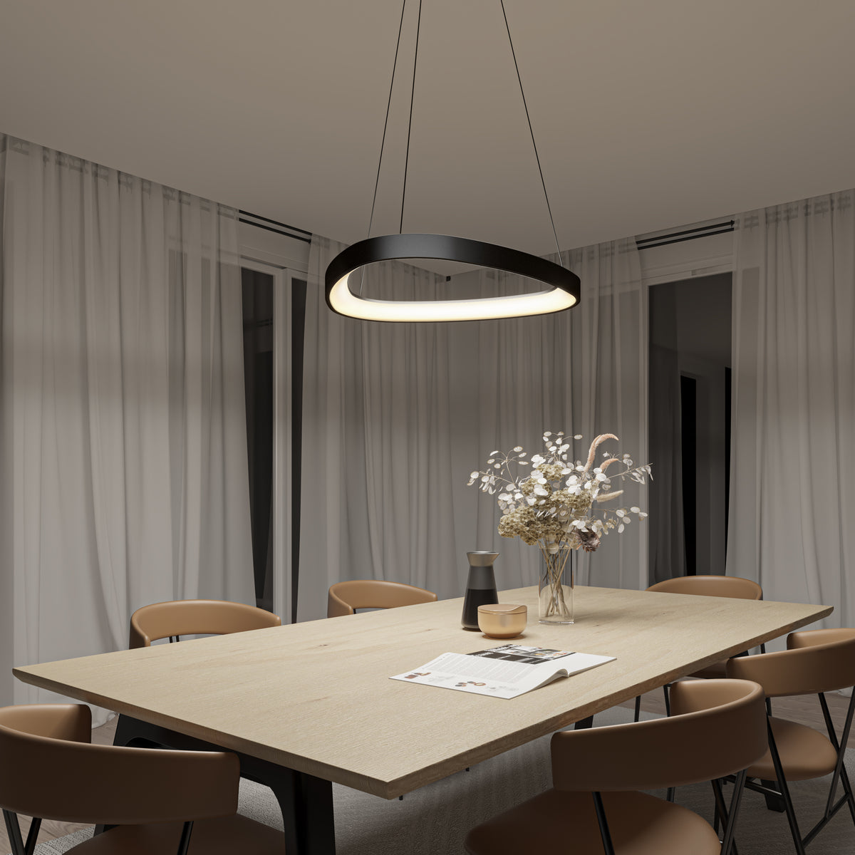 A modern dining room with a wooden table, tan chairs, a vase of dried flowers, and papers. Sheer curtains cover the windows, and a circular pendant light hangs above the table, creating a warm ambiance.