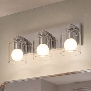 An Artika Aryna 20 in. 3-Light LED Wall Vanity 3000K with clear glass shades and glowing bulbs mounted above a mirror.