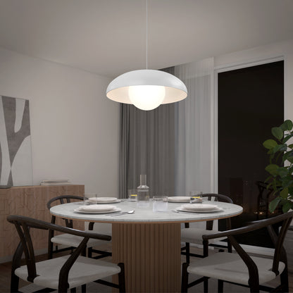 A modern dining room with a round table for four, black chairs, a large Boden LED modern mid-century pendant light by Artika overhead, a plant in the corner, and a window revealing the night sky.
