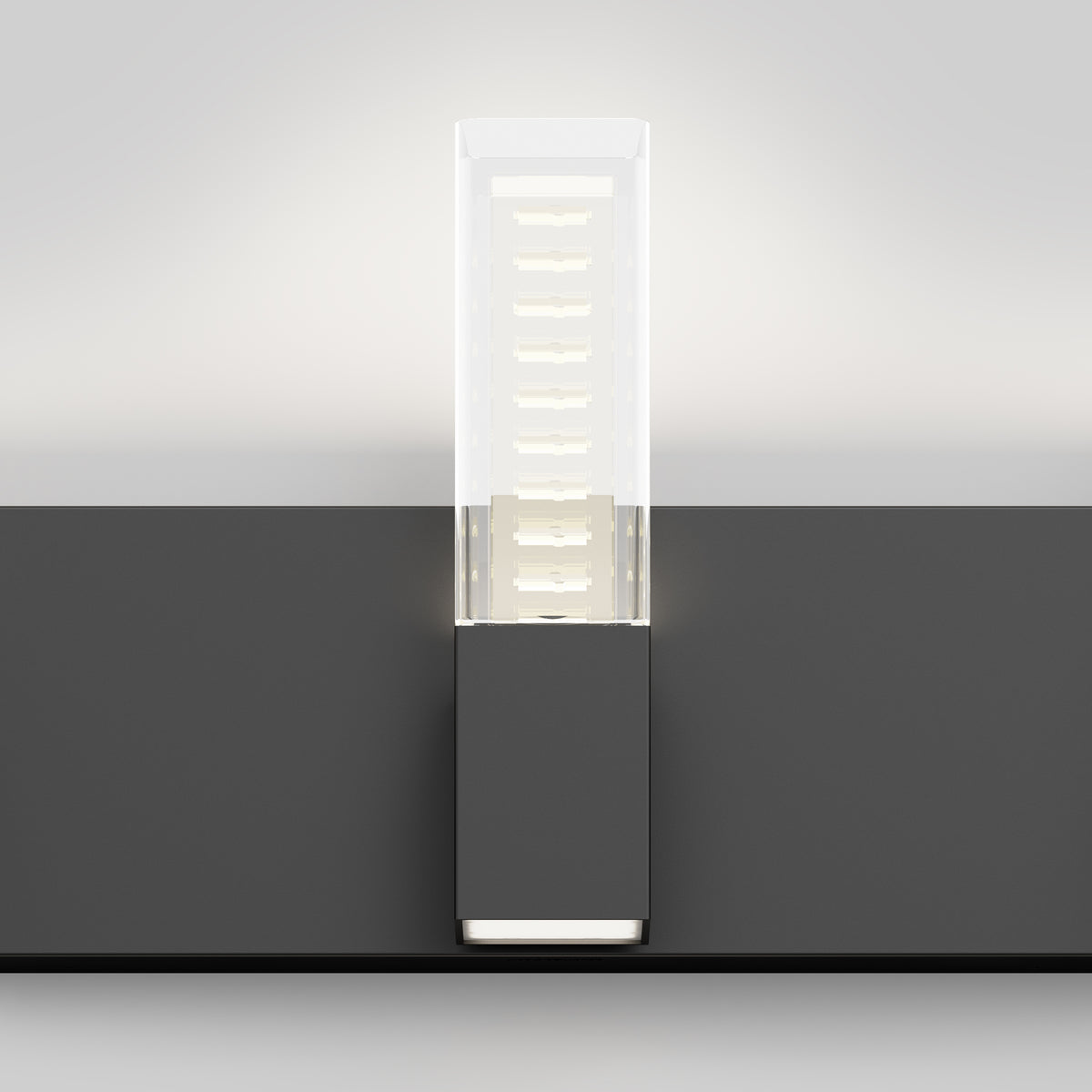 A modern wall-mounted LED light fixture with a rectangular frosted glass shade and a dark gray base, casting a soft glow upward on a light gray wall.