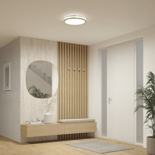 Modern entryway with a round mirror, wooden bench, coat hooks, potted plant, and Artika Hemisphere 15 in. LED ceiling light above the door.