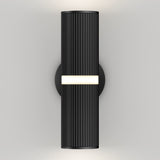 A modern black wall sconce with vertical grooves, mounted on a round base, emits light from a central horizontal strip and from the top and bottom edges, creating a sleek and minimalist lighting effect.