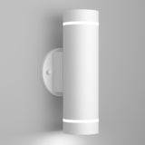 A modern cylindrical white wall sconce emits light from both the top and bottom, mounted on a round base against a plain light gray wall.