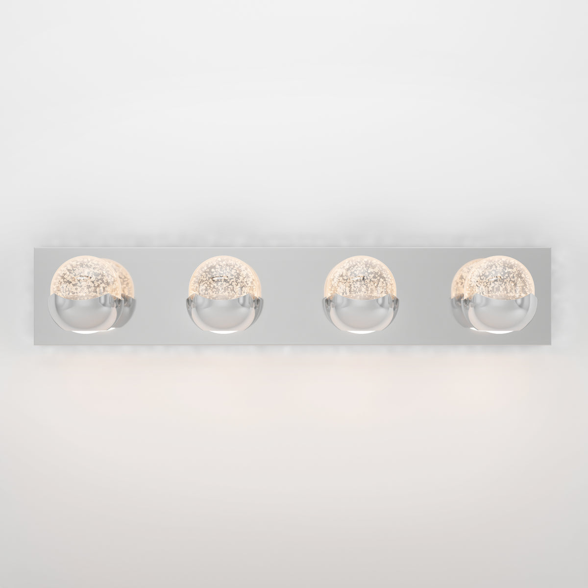 A modern wall-mounted light fixture with a rectangular chrome base and four round, illuminated glass globes evenly spaced in a row. The globes have a textured inner surface, casting a soft glow.