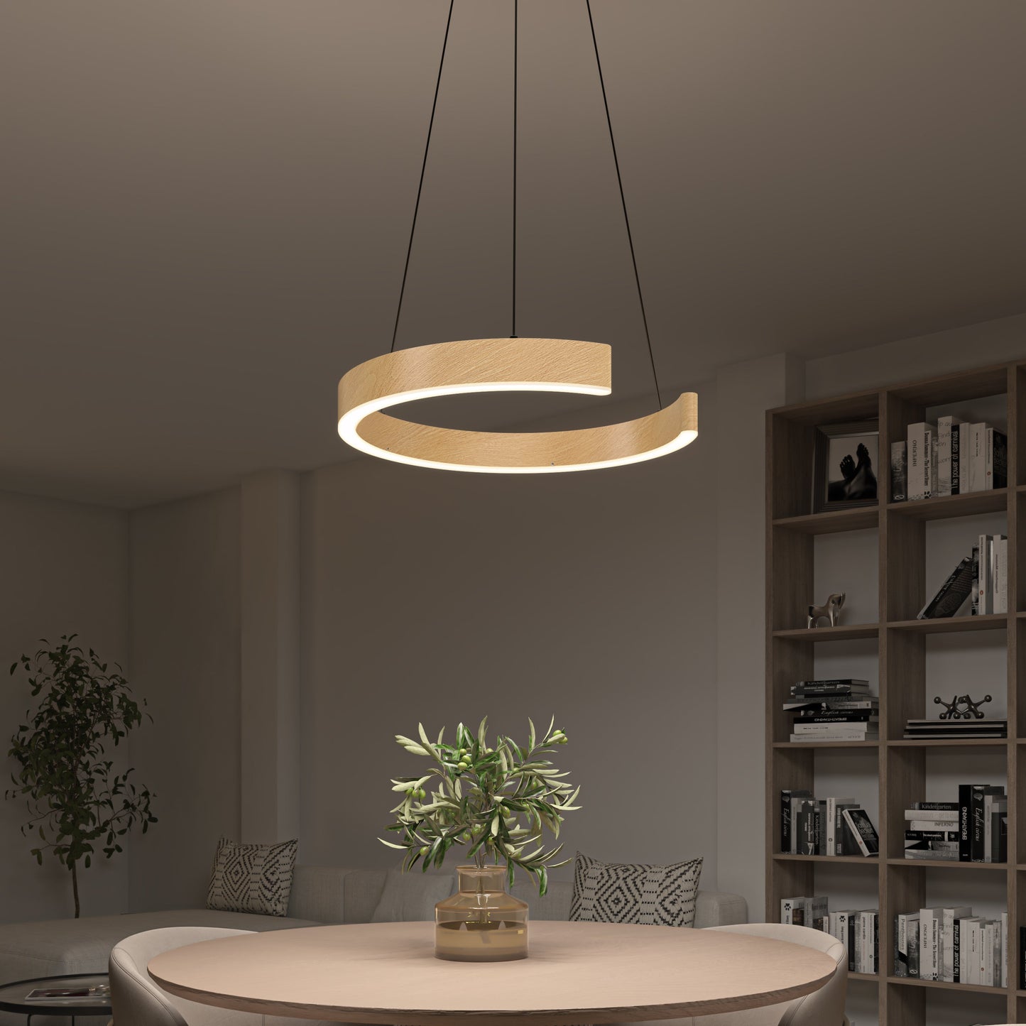 A modern living room features the Artika-CAN-dev Vance modern LED pendant light 3 CCT with dimmer compatibility above a round table with a potted plant, plus a bookshelf and partially visible sofa in the background.