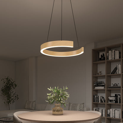A modern living room features the Artika-CAN-dev Vance modern LED pendant light 3 CCT with dimmer compatibility above a round table with a potted plant, plus a bookshelf and partially visible sofa in the background.