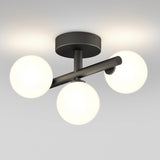 A modern ceiling light fixture with three frosted glass globe bulbs arranged on black metal arms, emitting a soft, even glow against a white ceiling.