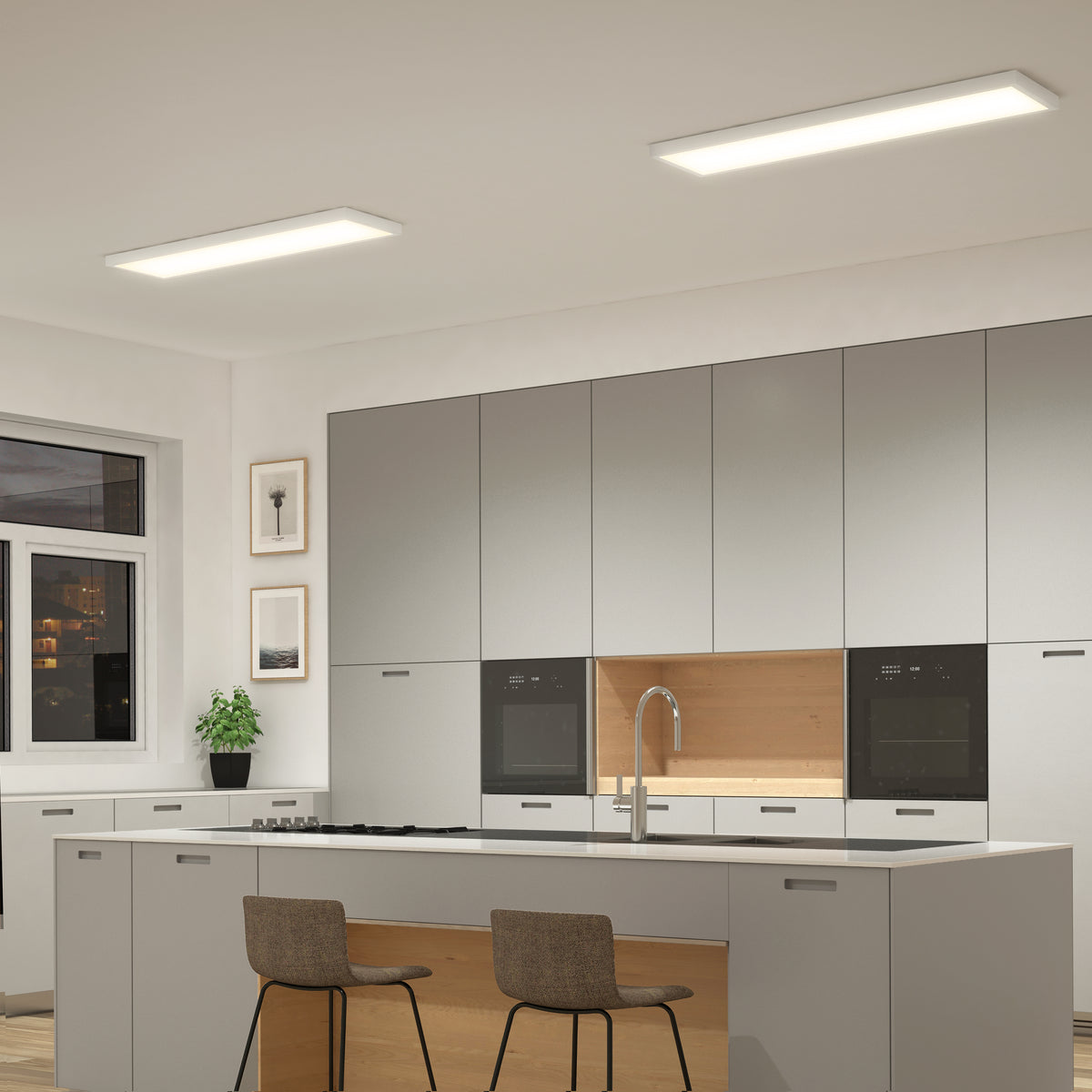 Modern kitchen with gray cabinets, island, built-in ovens & Artika Skyshade smart RGB LED panel above. Plant & art on the left.