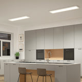 Modern kitchen with gray cabinets, built-in ovens, a central island with a sink, two brown chairs, potted plant by the window, framed art on the wall, and two rectangular ceiling lights.