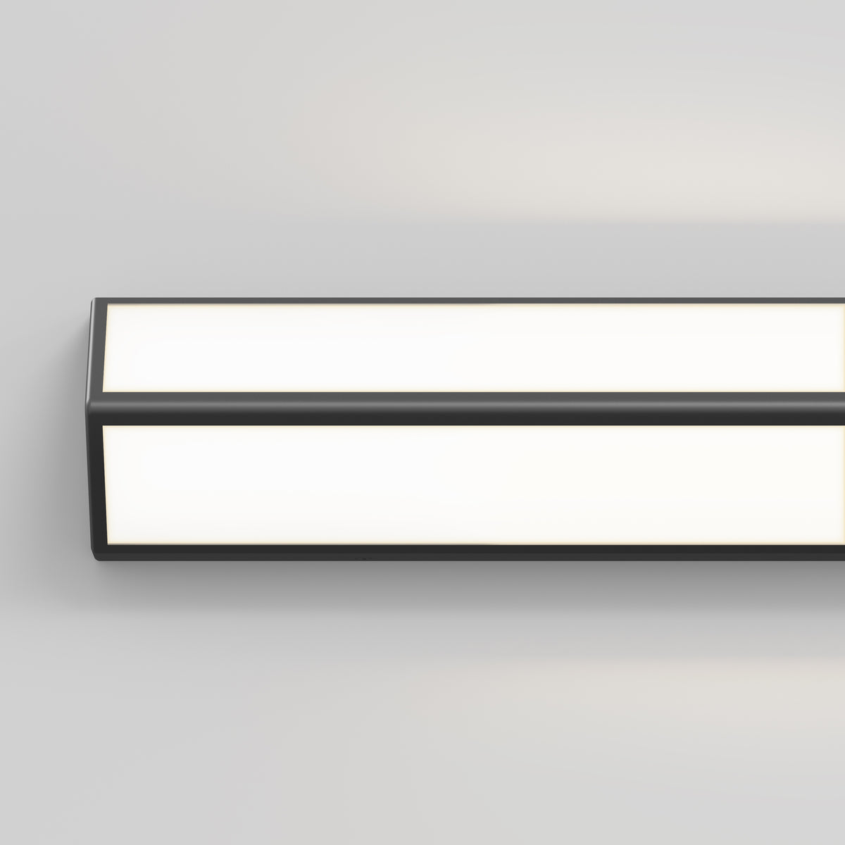 A modern, rectangular wall-mounted LED light fixture with a black frame, glowing with a bright white light against a plain light gray wall.
