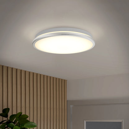 The Artika Vera 13 in. LED modern flush mount light with a chrome finish emits warm light in a room featuring a white ceiling, slatted light wood wall, door, and green leafy plant visible in the corner.
