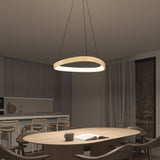 Modern dining room with a round wooden table, six chairs, a cup, and an open book. An illuminated circular pendant light hangs above. The background shows a minimalist kitchen and large window with sheer curtains at night.