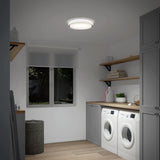 A modern laundry room with a washer and dryer side by side, grey cabinets, wooden countertops, shelves with folded towels, a laundry basket, and a window letting in natural light.