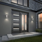Modern front entrance with a sleek black double door featuring horizontal glass panels, flanked by two wall-mounted lights. The exterior wall is gray with stone accents, and there are concrete steps leading to the door.