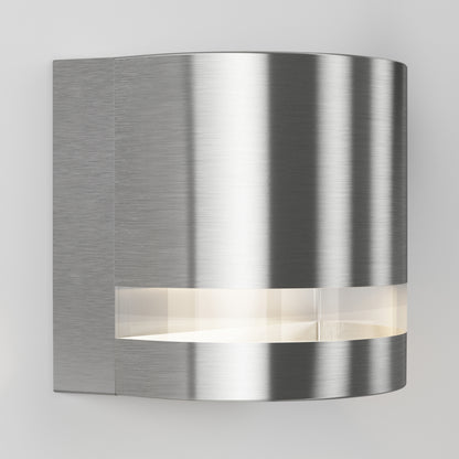 The Artika Valor Round LED indoor-outdoor wall light features a modern brushed metal finish, a curved rectangular design, and a horizontal LED strip near the bottom, shown mounted on a light-colored wall.