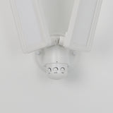 A close-up view of a modern white double LED security light fixture, mounted on a wall, with adjustable panels and three control dials labeled LUX, SENS, and TIME.