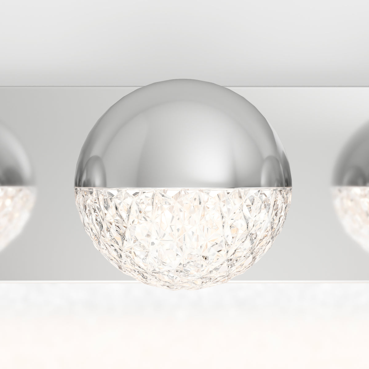 A close-up of a modern ceiling light fixture with a half-sphere design; the top half is smooth, shiny silver, and the bottom half is faceted clear glass, emitting a sparkling glow.