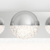 A close-up of a modern ceiling light fixture with a half-sphere design; the top half is smooth, shiny silver, and the bottom half is faceted clear glass, emitting a sparkling glow.