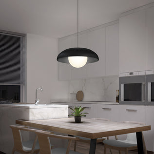 A modern kitchen features white cabinets, a marble backsplash, a built-in oven, and a wooden dining table with four chairs. A potted plant sits on the table beneath the Artika Boden LED modern mid-century pendant light (3 CCT).