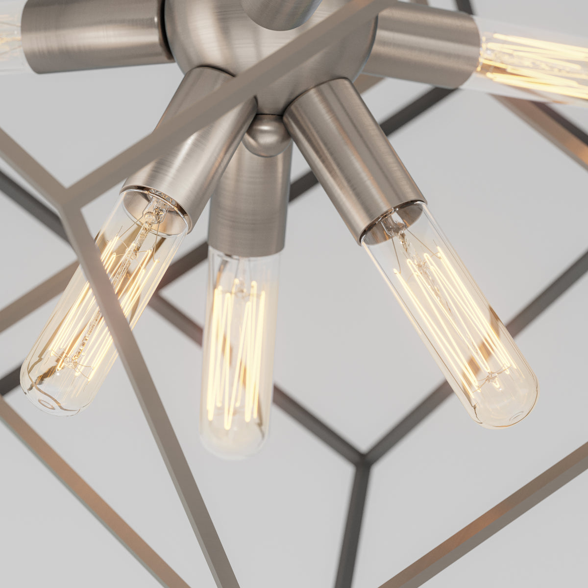 Close-up of a modern ceiling light fixture with exposed filament bulbs and a geometric metal frame, viewed from below. The fixture has a brushed metal finish and emits a warm glow.