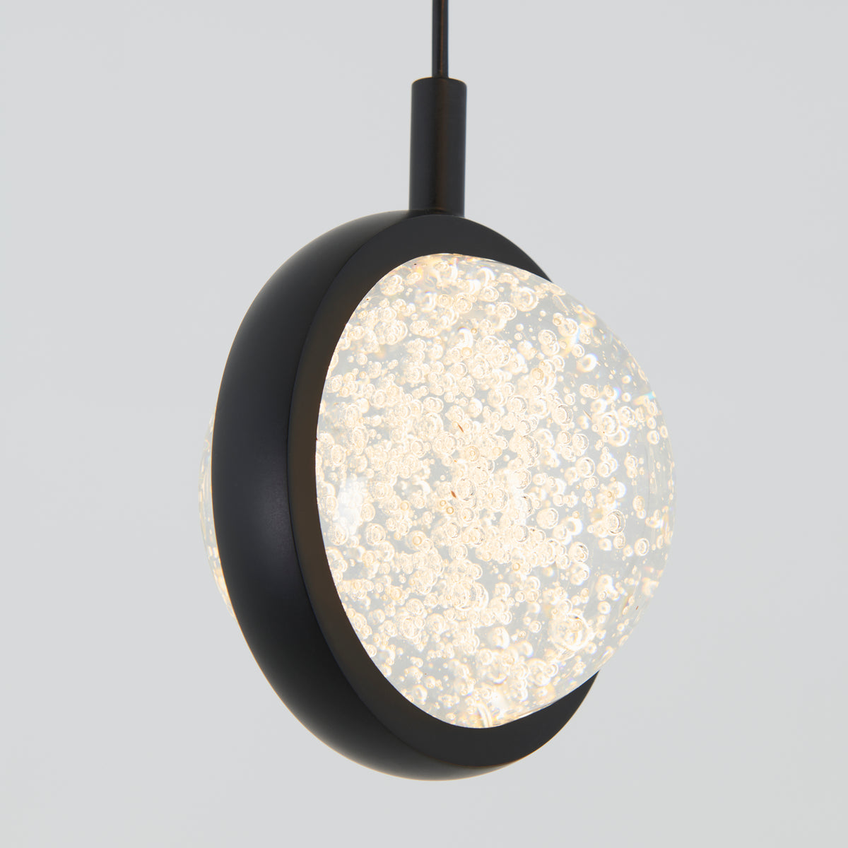 A modern pendant light with a black circular frame surrounding a textured, illuminated glass globe filled with small bubbles, hanging against a plain light gray background.