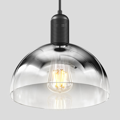 The Artika Nella Pendant without Bulbs features a clear glass shade and black perforated metal fixture, showcasing a visible filament bulb, all set against a plain gray background.