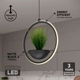 A modern pendant light with a circular LED frame and a hanging plant in the center, featuring matte black finish, adjustable height, energy efficiency, and a 3-year warranty. Marble wall background.