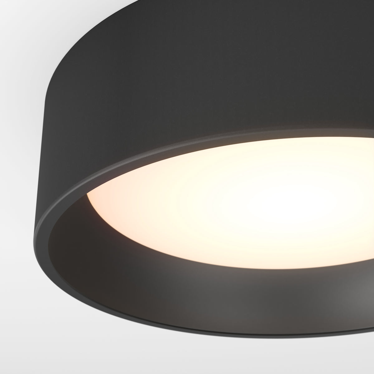 A close-up of a modern black ceiling light fixture with a glowing white bulb, set against a plain white background.