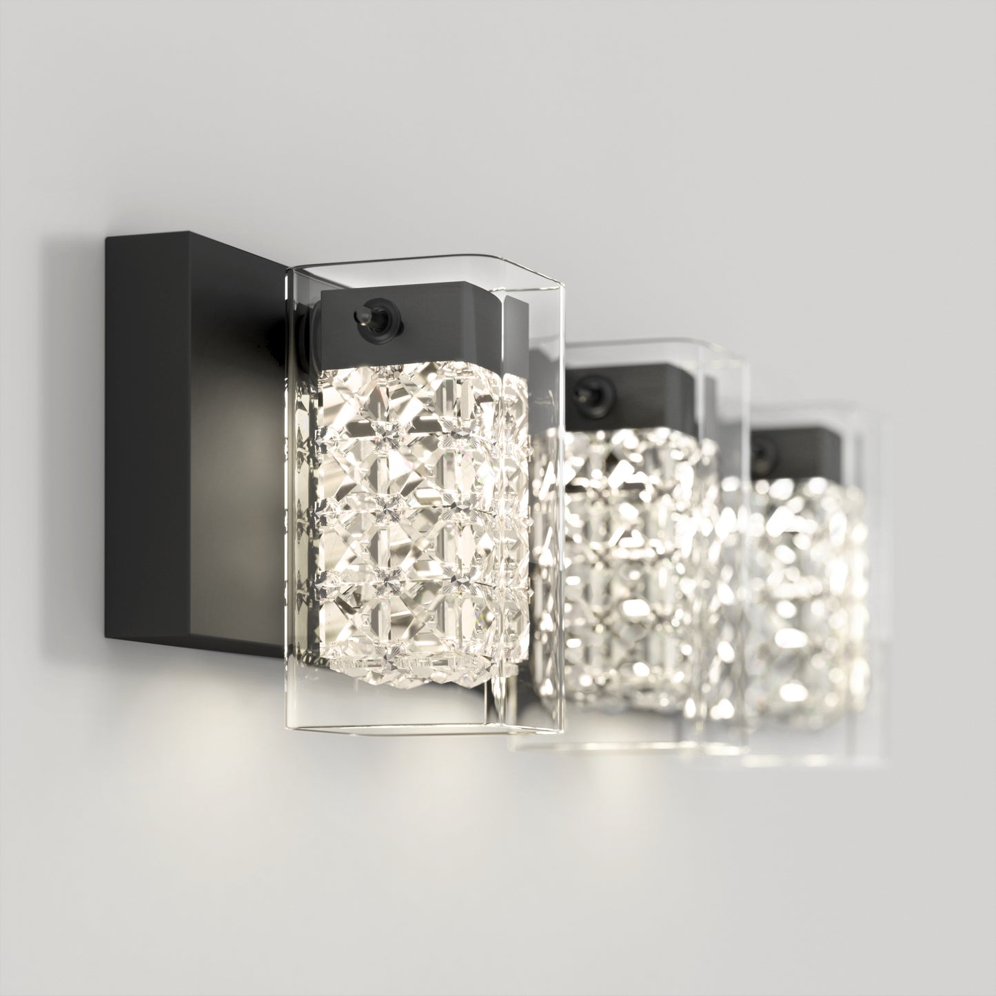 Three Artika Crystal Cube LED bathroom vanity lights, wall-mounted with black bases and clear textured glass shades, emit bright white light against a light-colored wall.