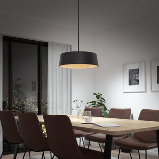 A modern dining room featuring a wooden table, six brown upholstered chairs, the Artika Alton modern LED pendant light 5 CCT in black, framed art on white walls, a potted plant, and a window overlooking the city at night.