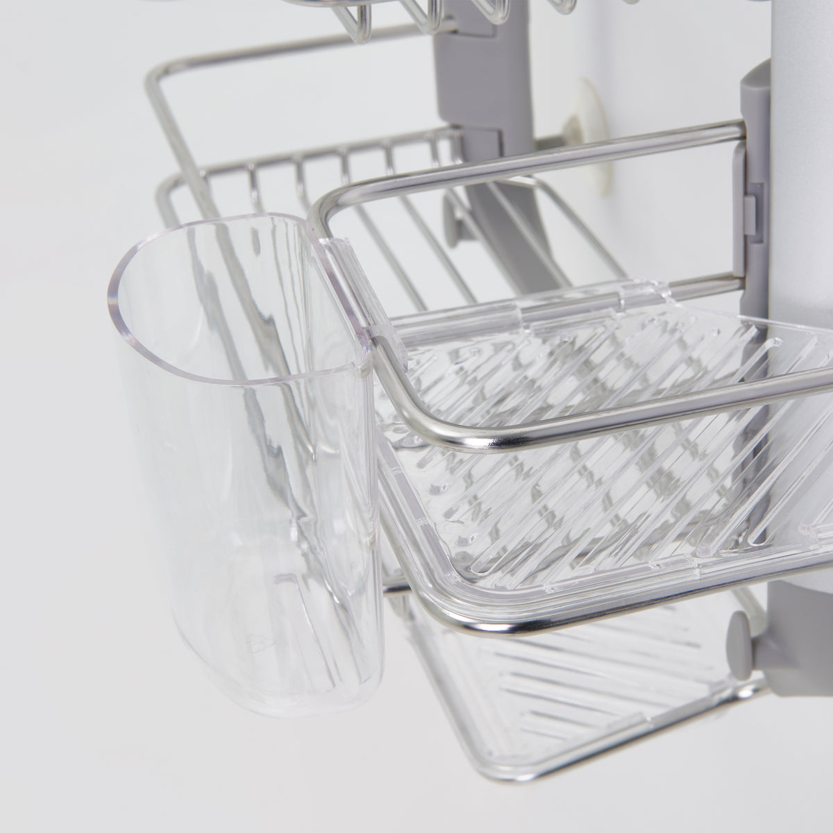 Close-up of a metal and plastic kitchen rack with a clear plastic cup and tray, designed for organizing utensils and draining water, attached to a vertical rod.