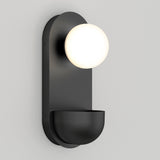 A modern black wall sconce with a rounded base and a frosted white globe light mounted above a semicircular dish, set against a plain light gray wall.