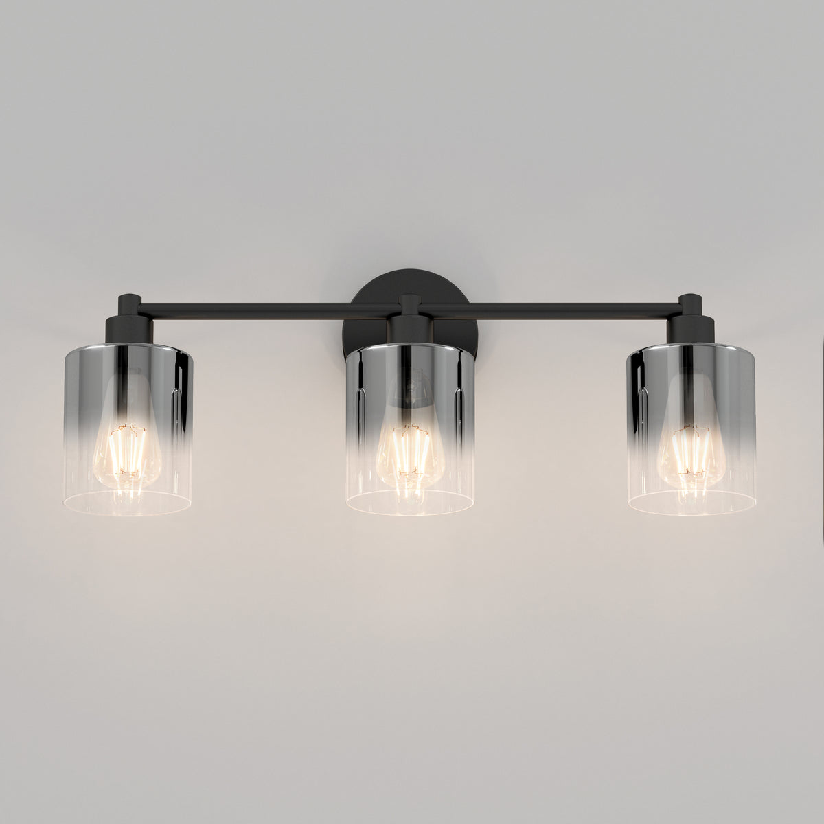 A modern wall sconce light fixture with three exposed bulbs, each enclosed in a clear cylindrical glass shade, mounted on a black horizontal bar against a light gray wall.