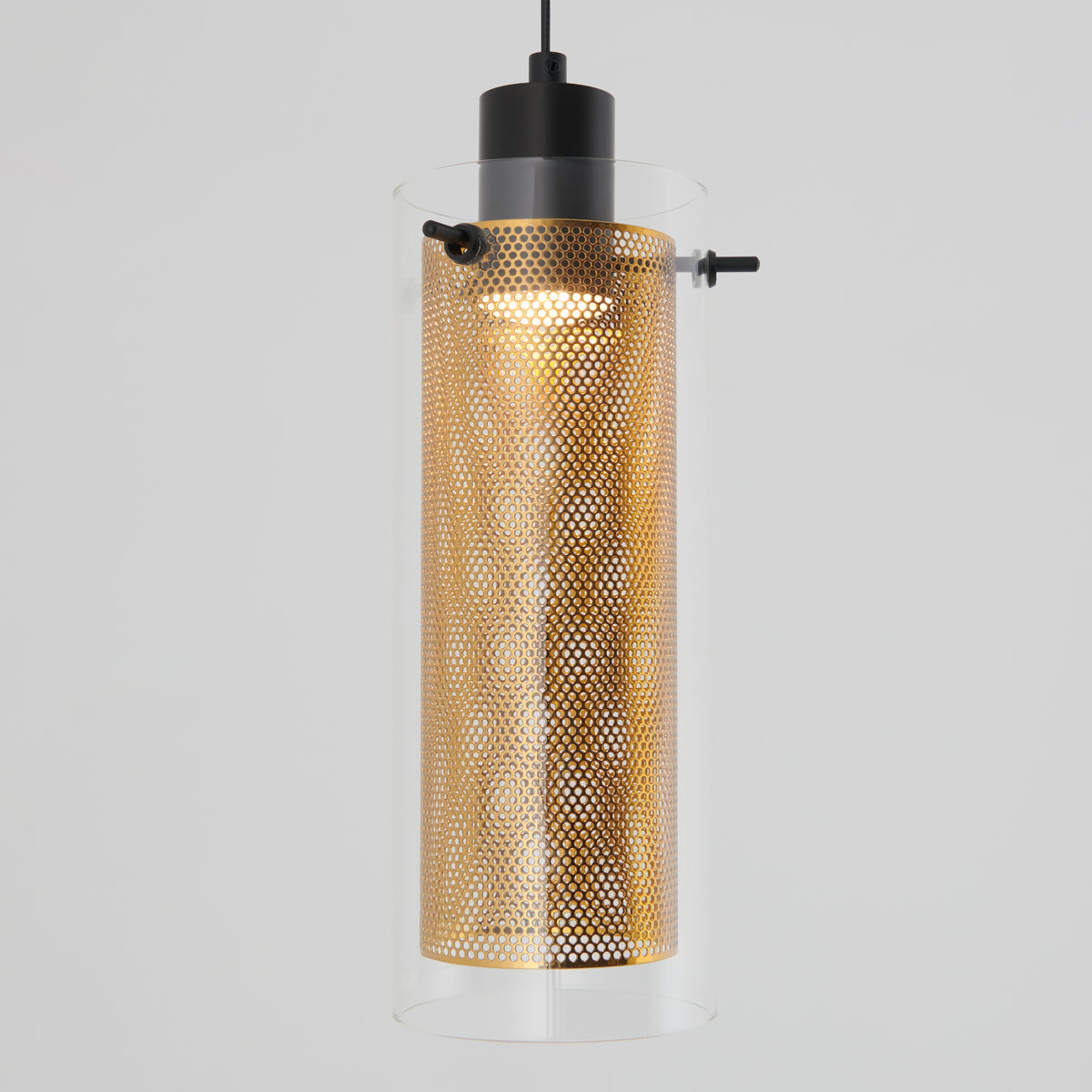 The Artika Oxion 1-light LED pendant features a cylindrical clear glass shade and a perforated gold metal inner cylinder, suspended by a black cord against a plain light gray background.