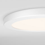 A close-up view of a modern, round, white ceiling light fixture with a soft glow, mounted on a smooth white ceiling.