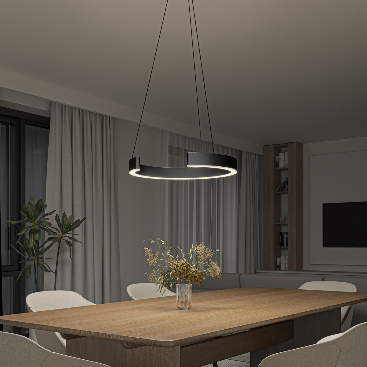 A modern dining room with a wooden table, beige chairs, a vase of dried flowers, and a circular pendant light hanging above. The room has large windows with curtains and a built-in shelving unit.