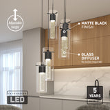 Modern kitchen with three cylindrical pendant lights featuring matte black finishes and glass diffusers, hanging above a countertop. Text highlights adjustable height, integrated LED, and a 5-year warranty.