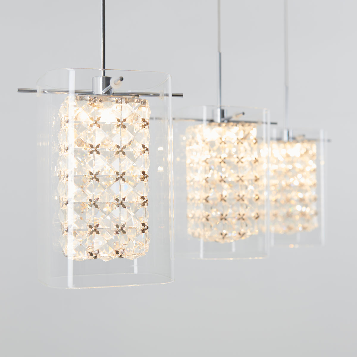 A row of modern pendant lights with clear glass shades and geometric crystal patterns, hanging from the ceiling against a light gray background.