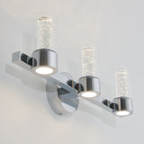 A modern wall-mounted light fixture with three cylindrical glass shades, each containing bubbles, mounted on a chrome base and arm, emitting a soft white light.