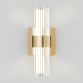 Artika’s Dorado contemporary LED wall sconce 3 CCT features a brushed gold base and vertical clear glass rods, casting a soft glow on light gray walls—an elegant luxury fixture for modern spaces.