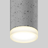 A close-up of a cylindrical ceiling light fixture with a gray, speckled, concrete-like texture and a softly glowing white light against a plain light gray background.